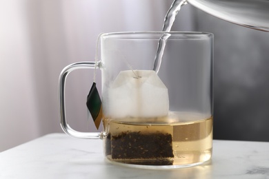 Photo of Pouring hot water into glass cup with tea bag on table