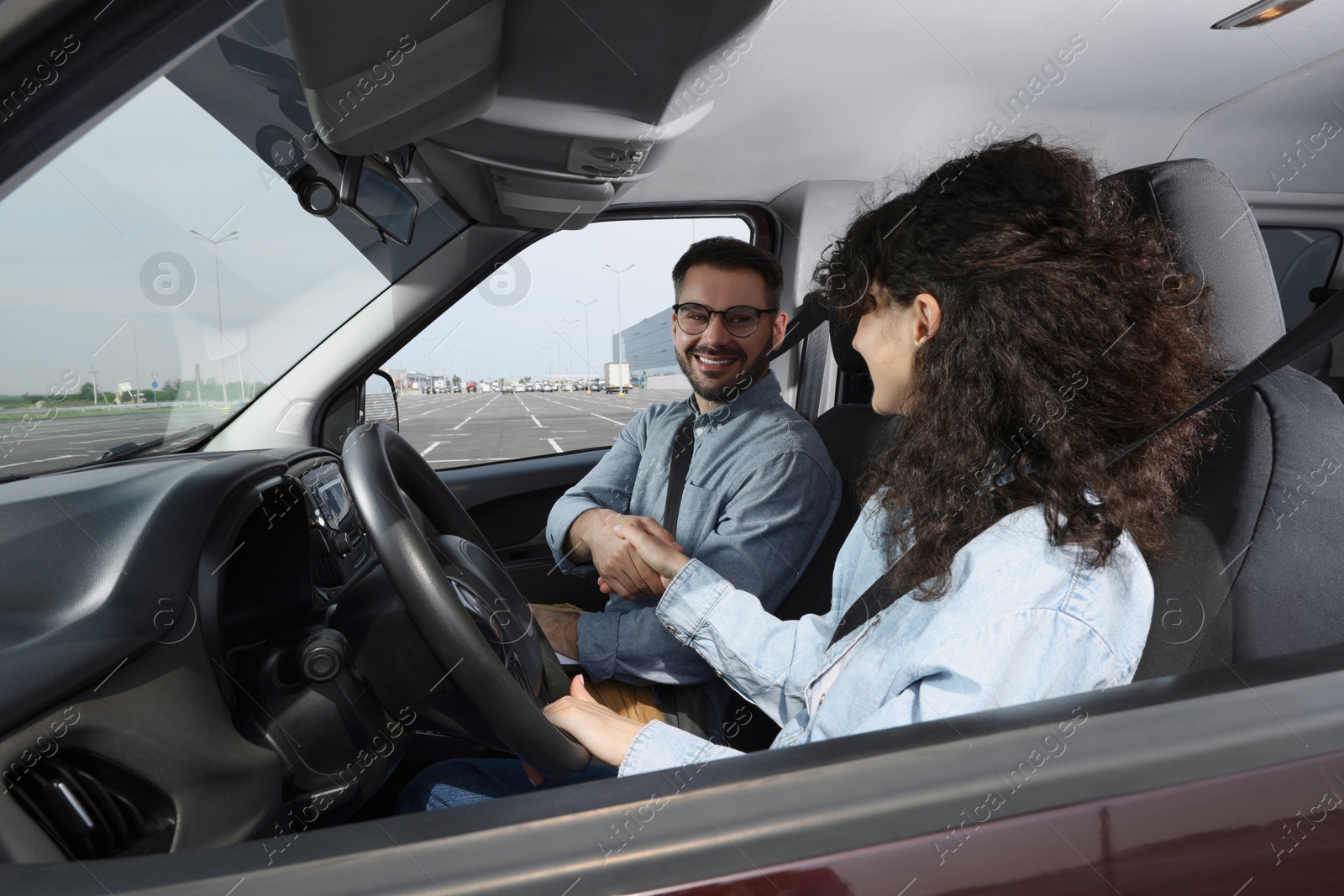 Photo of Driving school. Happy student shaking hands with driving instructor during lesson in car at parking lot