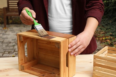 Photo of Man applying wood stain onto crate at table outdoors, closeup