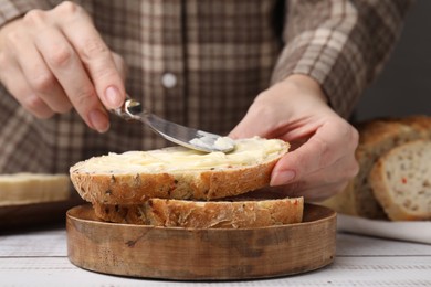 Photo of Woman spreading butter onto bread at white wooden table, closeup