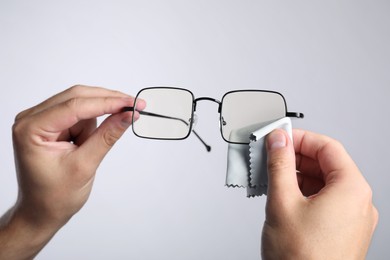 Photo of Man wiping glasses with microfiber cloth on light grey background, closeup