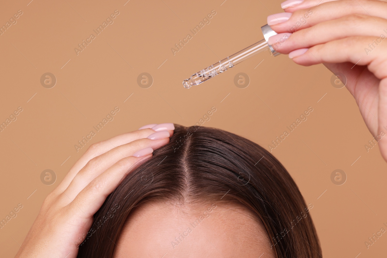 Photo of Woman applying serum onto hair on beige background, closeup