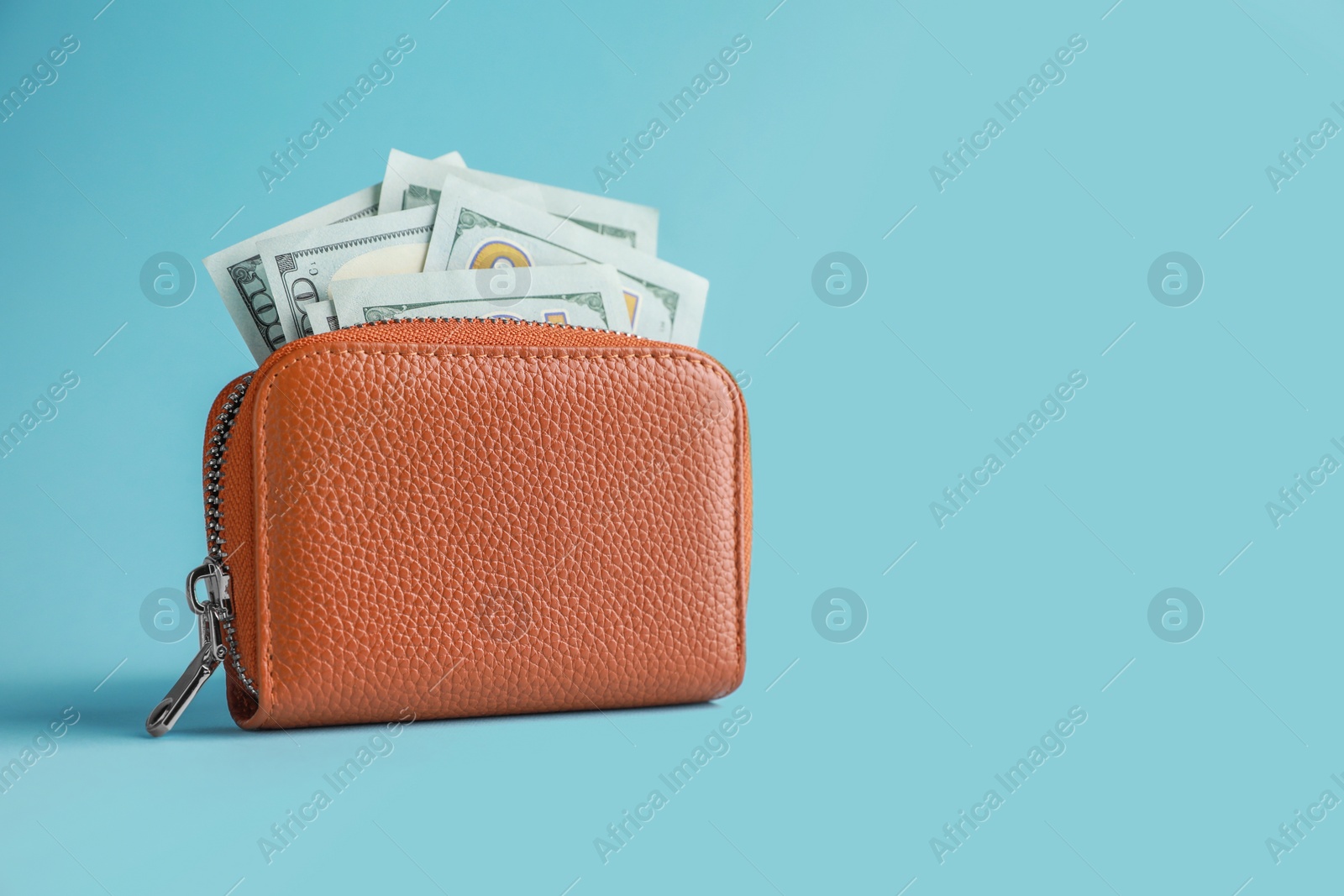 Photo of One open leather purse with money on light blue background. Space for text