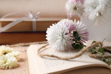 Book with chrysanthemum flowers as bookmark on beige textured table, closeup. Space for text