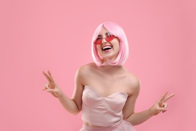 Photo of Pink look. Funny girl in wig and top wearing bright sunglasses on color background
