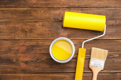 Photo of Flat lay composition with can of yellow paint, brush and roller on wooden background. Space for text