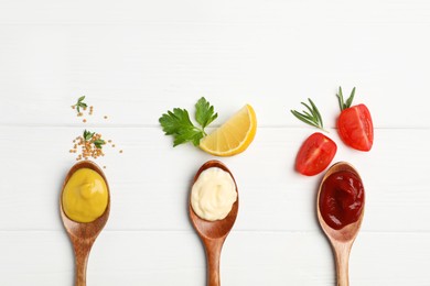 Photo of Ketchup, mayonnaise, mustard in spoons and ingredients on white wooden table, flat lay