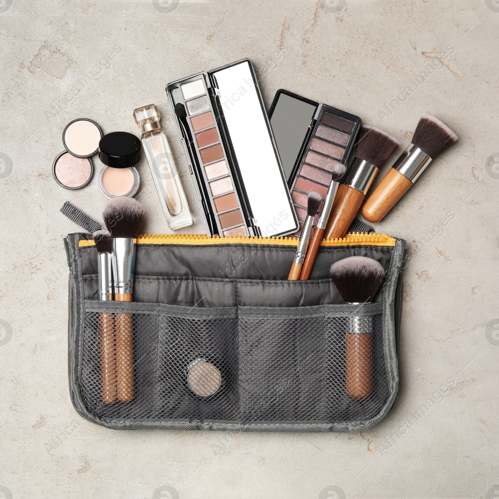 Photo of Cosmetic bag with makeup products on light grey stone background, flat lay