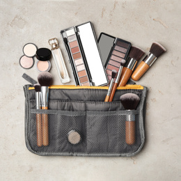 Photo of Cosmetic bag with makeup products on light grey stone background, flat lay