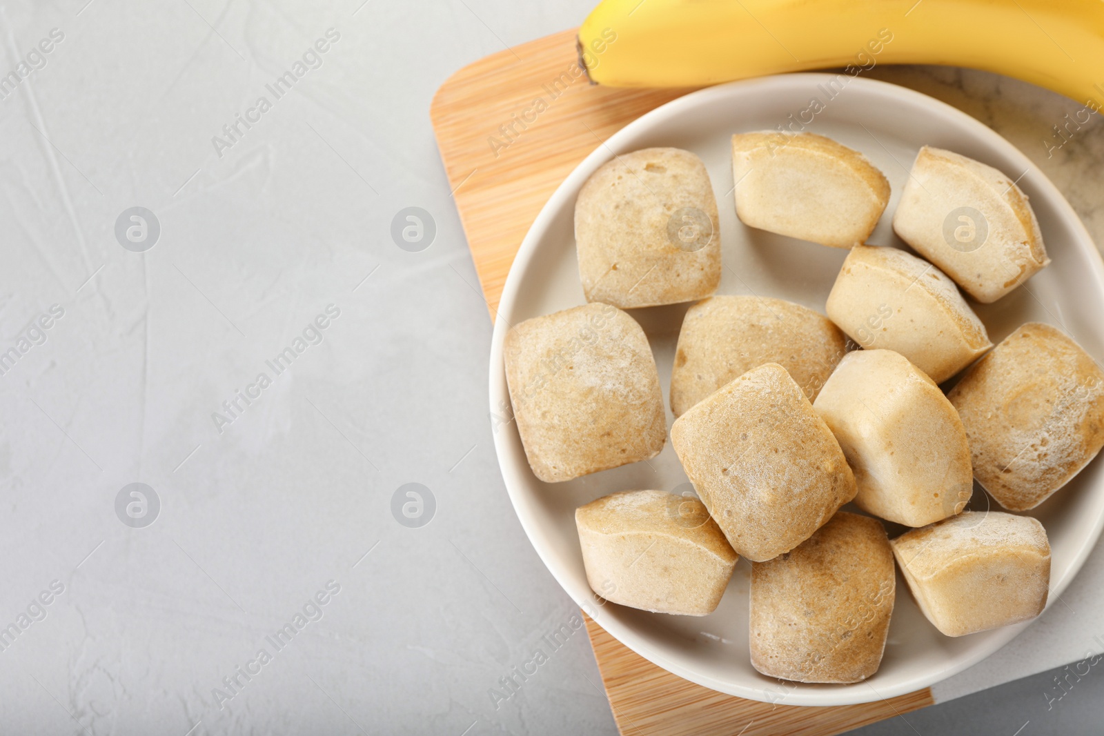 Photo of Frozen banana puree cubes and ingredient on light grey table, top view. Space for text