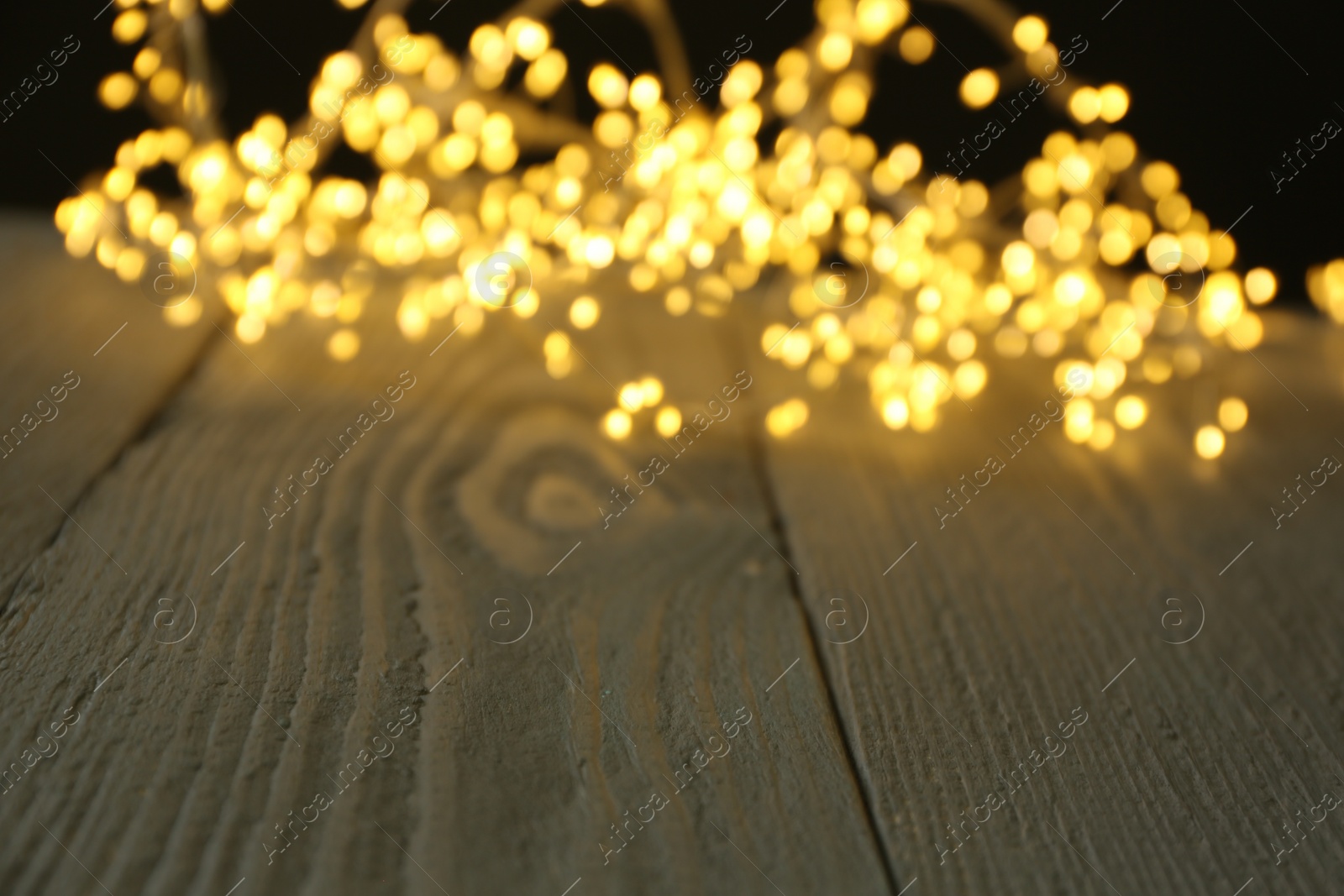 Photo of Beautiful glowing Christmas lights on wooden surface, blurred view