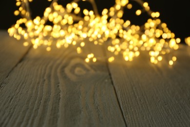 Photo of Beautiful glowing Christmas lights on wooden surface, blurred view