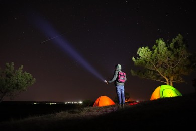 Image of Man with bright flashlight near camping tents outdoors at night
