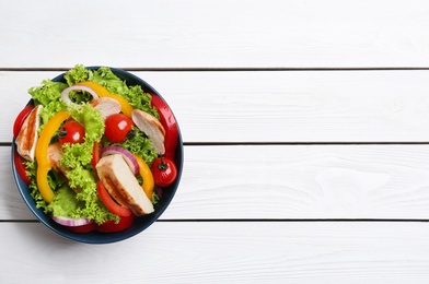 Photo of Delicious salad with chicken and vegetables on white wooden table, top view. Space for text