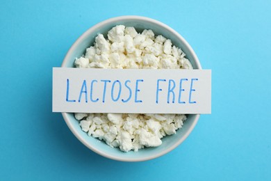 Photo of Cottage cheese and card with phrase Lactose free on light blue table, top view