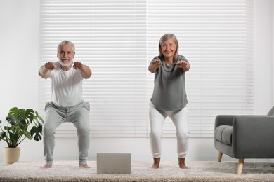 Photo of Senior couple practicing yoga with laptop on carpet at home