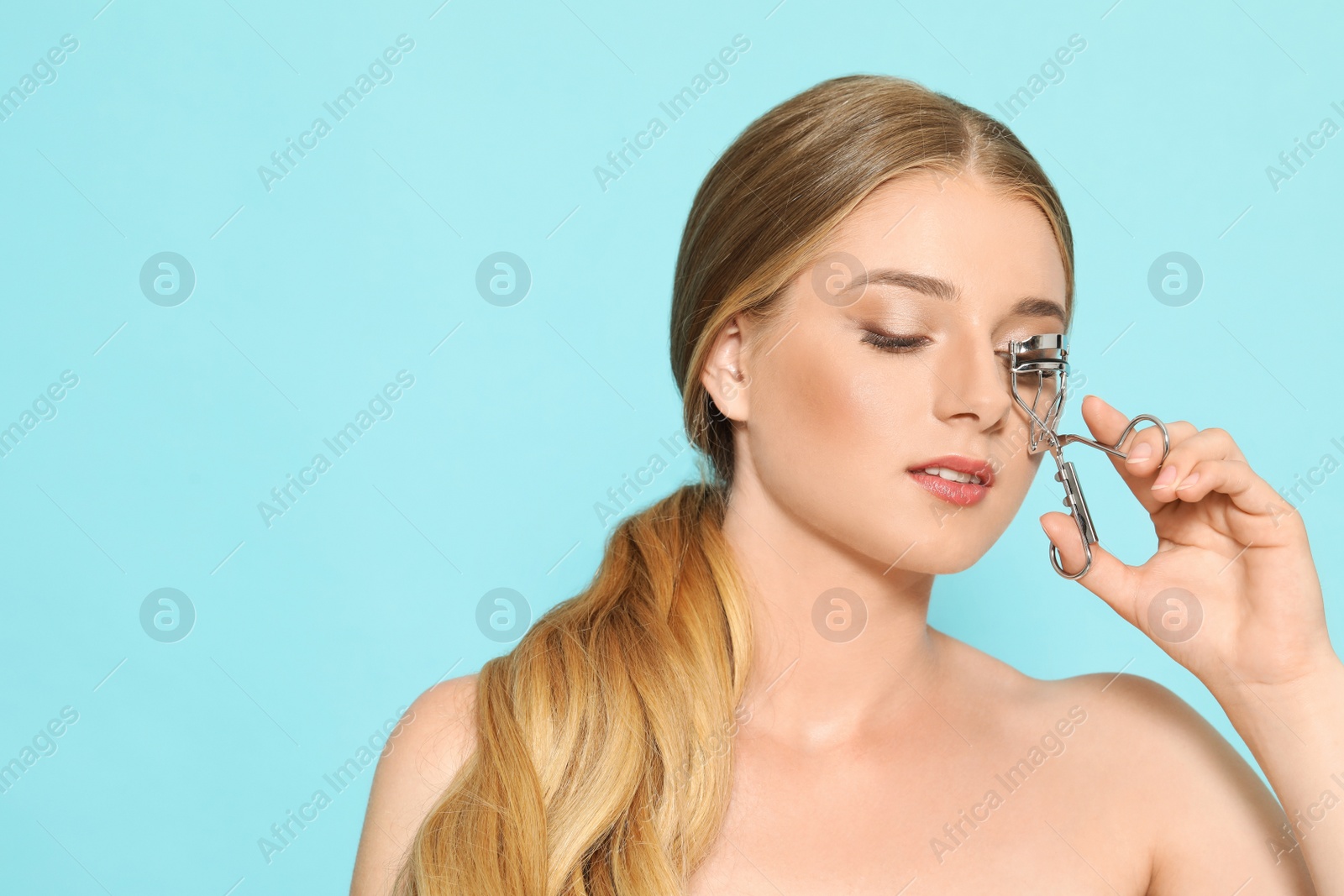 Photo of Young woman using eyelash curler on light blue background. Space for text