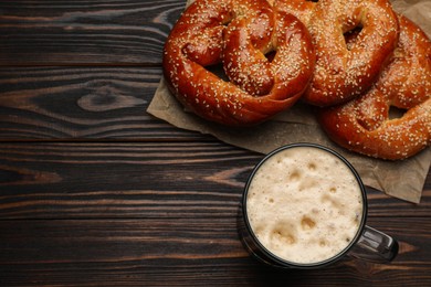 Photo of Tasty freshly baked pretzels and mug of beer on wooden table, flat lay. Space for text