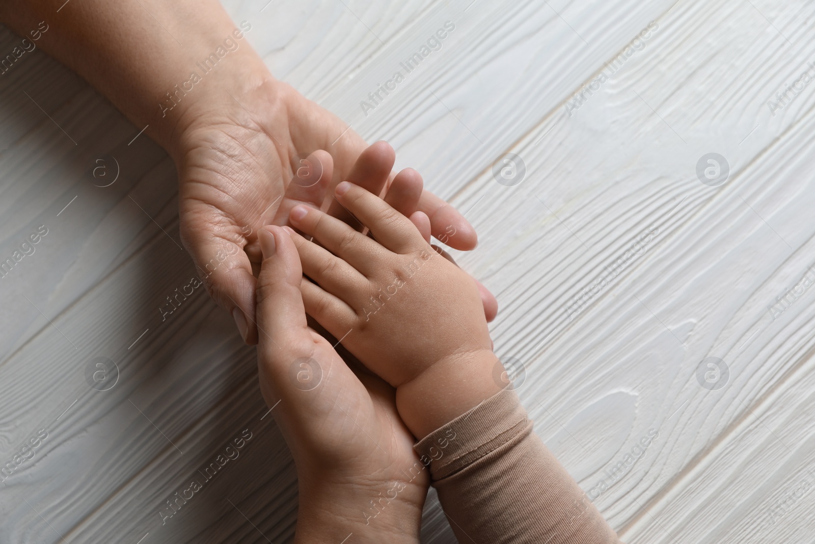 Photo of Family holding hands together at white wooden table, top view. Space for text