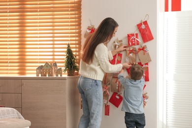 Mother and son taking gift from Advent calendar at home, back view. Christmas tradition