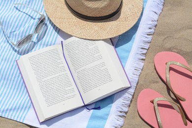 Photo of Beach towel with book, straw hat, sunglasses and flip flops on sand, flat lay