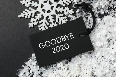 Flat lay composition with phrase Goodbye 2020 and artificial snow on black table