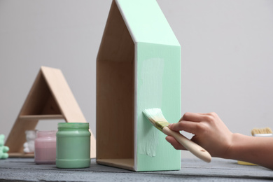 Photo of Woman painting wooden house model at grey table, closeup