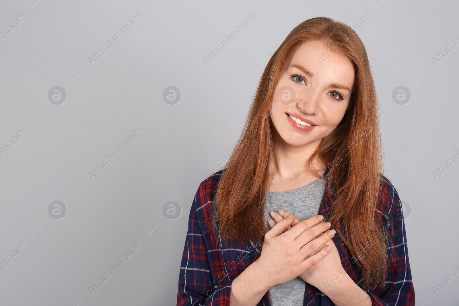 Photo of Beautiful grateful woman with hands on chest against light grey background. Space for text