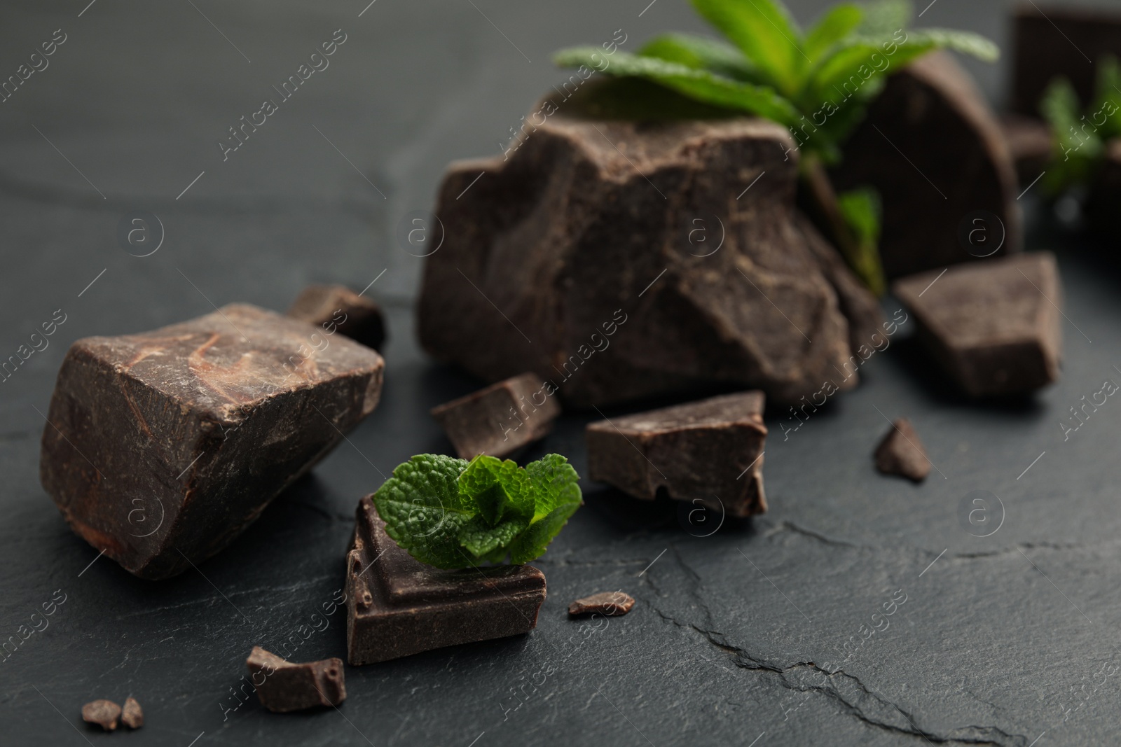 Photo of Tasty dark chocolate pieces with mint on black table, closeup