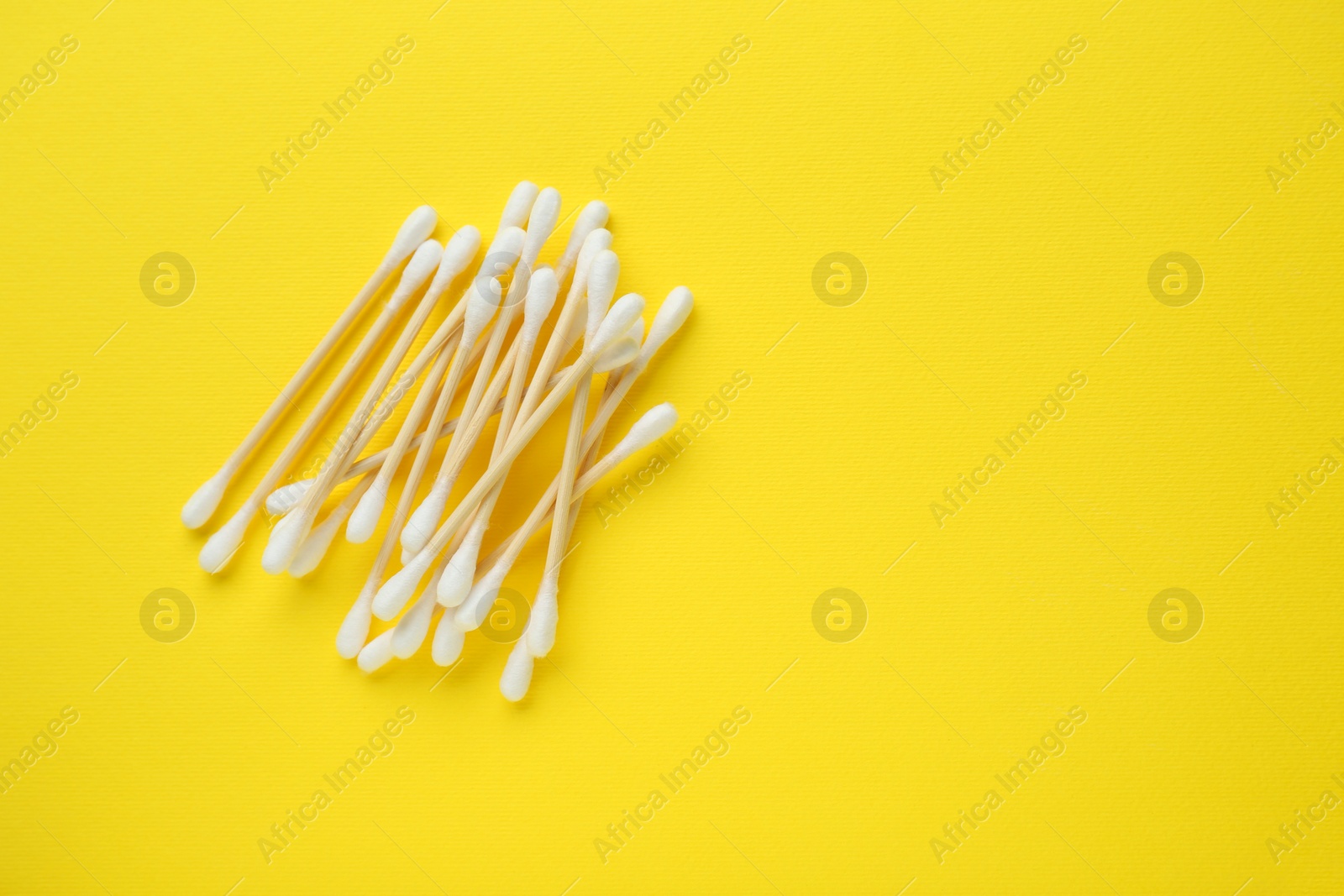 Photo of Heap of wooden cotton buds on yellow background, flat lay. Space for text