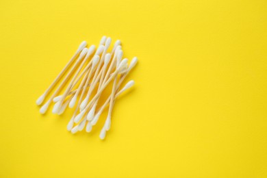 Heap of wooden cotton buds on yellow background, flat lay. Space for text