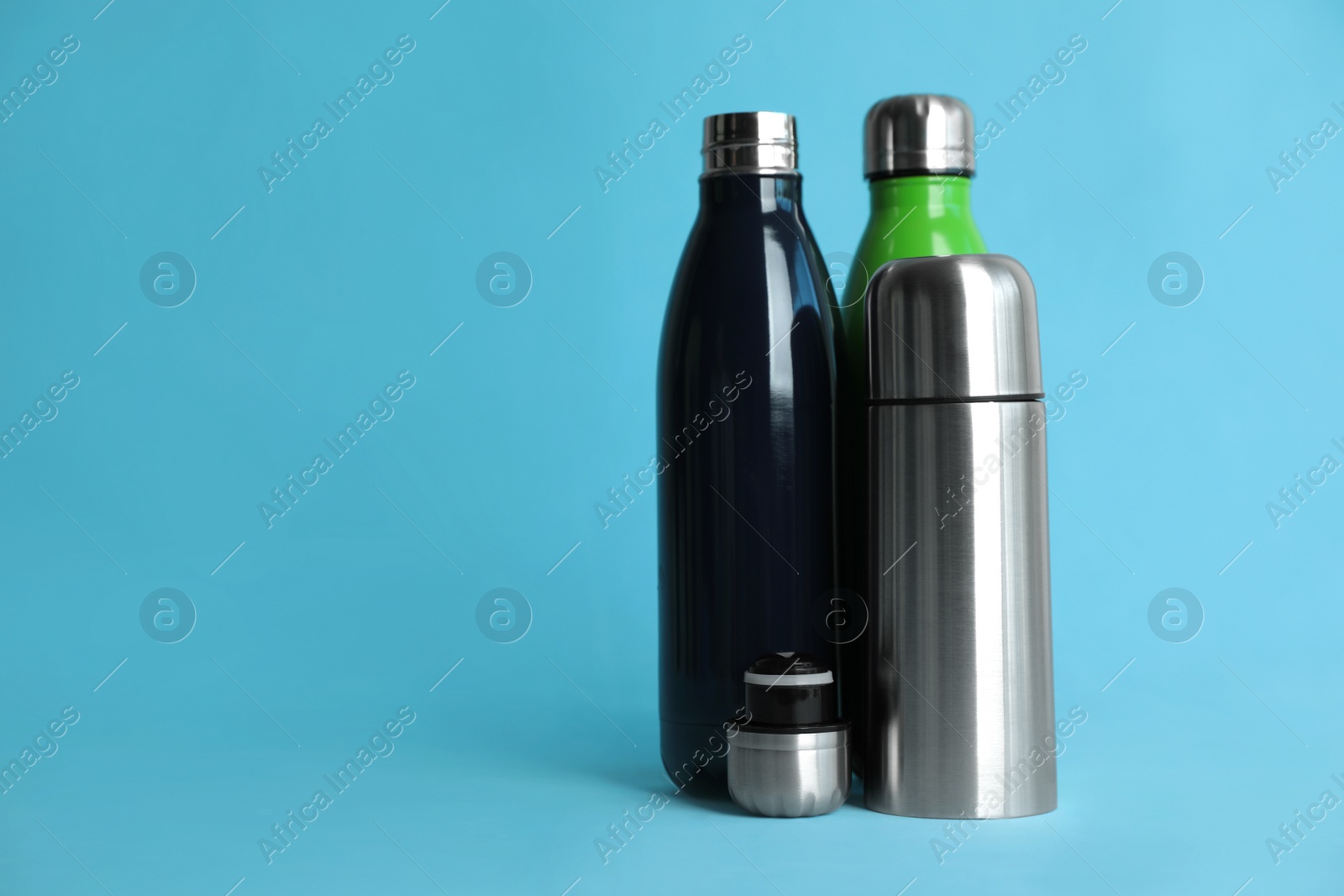 Photo of Stylish thermo bottles on light blue background, space for text