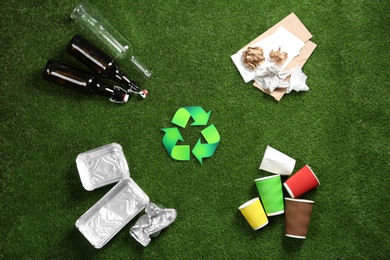 Flat lay composition with recycling symbol and different garbage on green grass