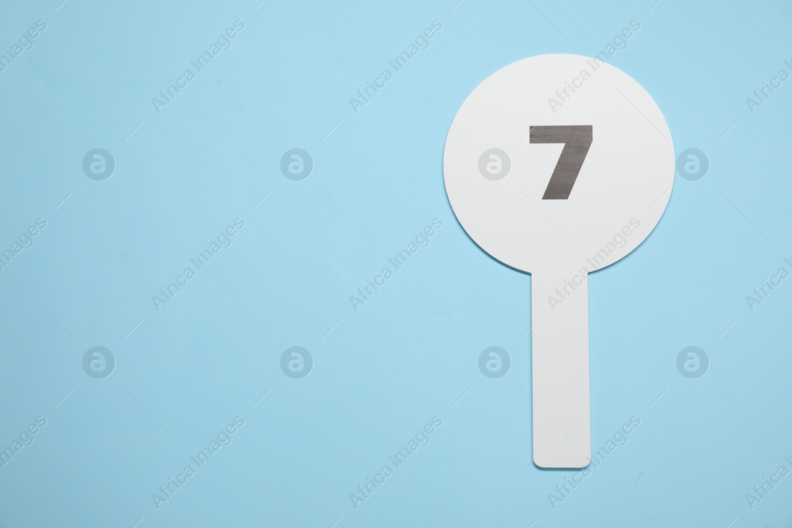 Photo of Auction paddle with number 7 on light blue background, top view. Space for text