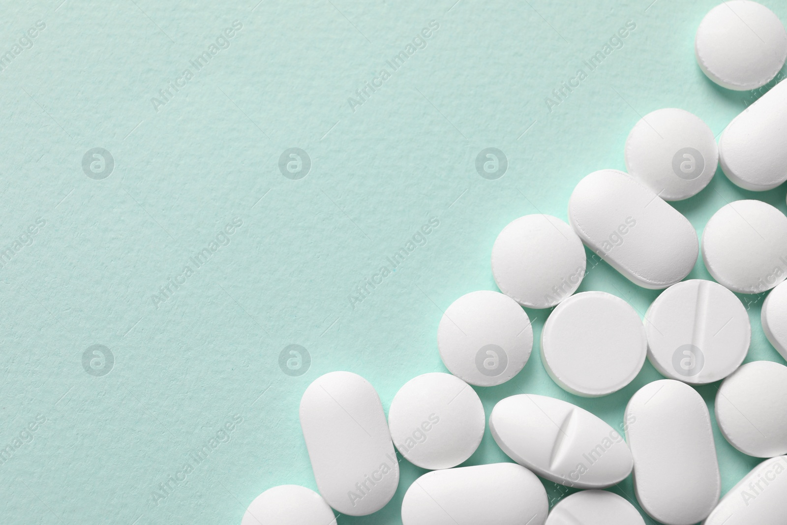 Photo of White pills on mint background, flat lay. Space for text