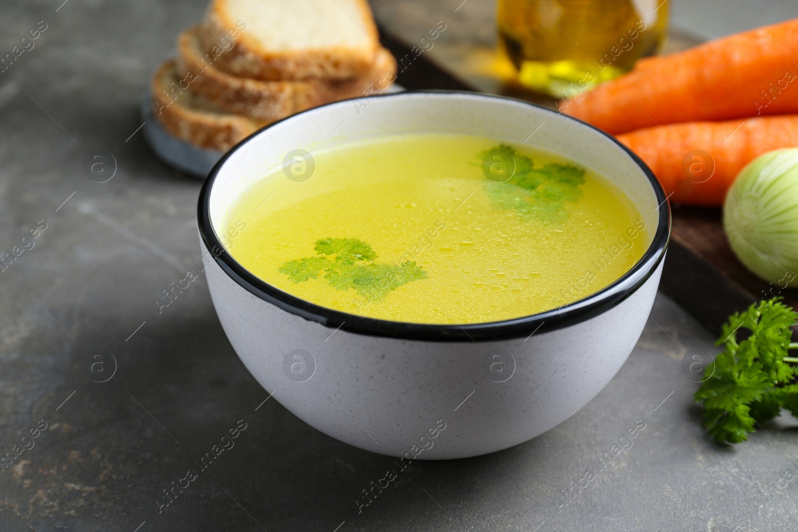 Photo of Delicious chicken bouillon and ingredients on grey table, closeup