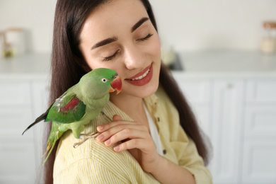 Photo of Young woman with Alexandrine parakeet indoors. Cute pet