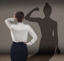 Image of Businesswoman and shadow of strong muscular lady in front of her on grey wall. Concept of inner strength