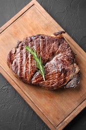 Wooden board with delicious fried beef meat and rosemary on grey textured table, top view