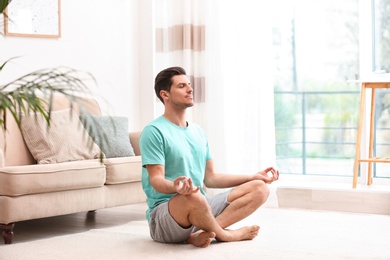Photo of Man meditating on floor in living room. Zen concept