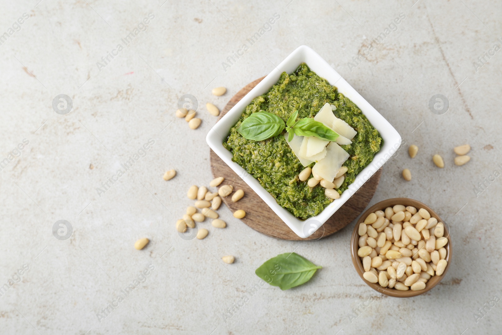 Photo of Bowl with delicious pesto sauce, cheese, pine nuts and basil leaves on light table, flat lay. Space for text