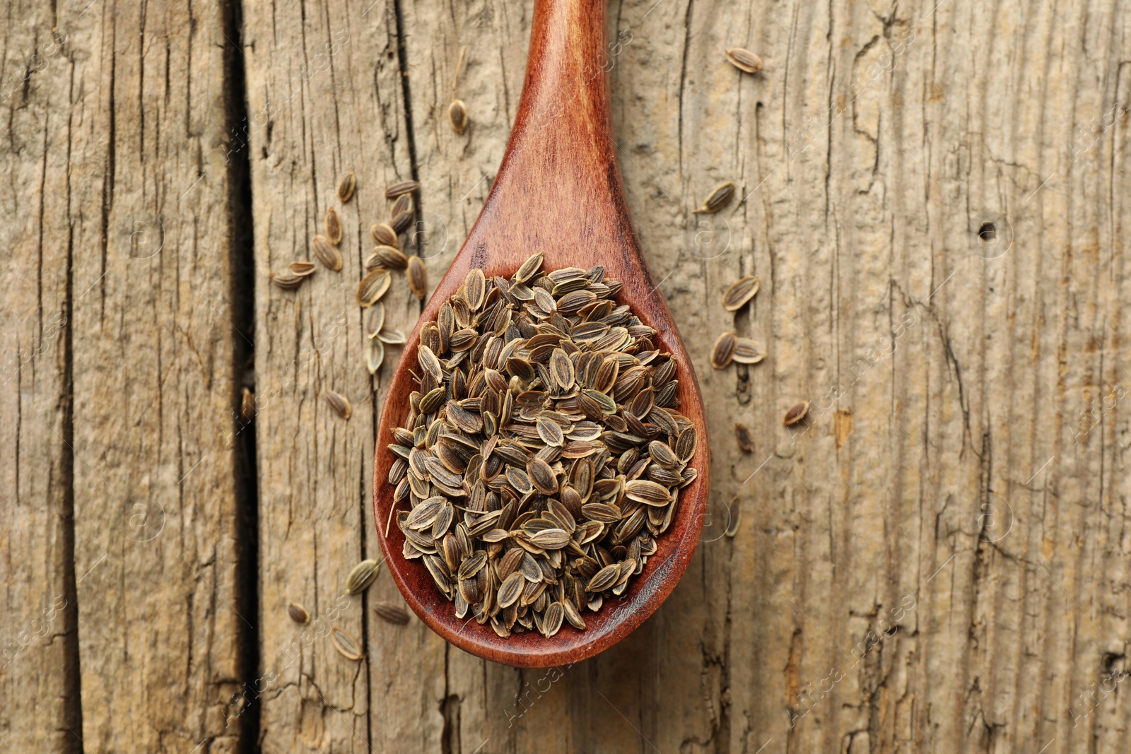 Photo of Spoon of dry dill seeds on wooden table, top view