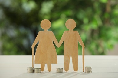 Pension savings. Figure of senior couple and coins on white table against blurred green background