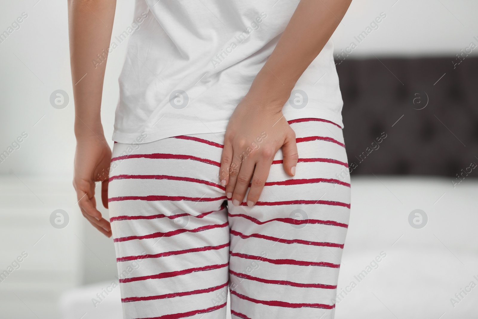 Photo of Young woman suffering from hemorrhoid in bedroom, closeup