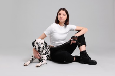 Beautiful young woman with her adorable Dalmatian dog on light grey background. Lovely pet