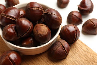 Photo of Bowl with roasted edible sweet chestnuts on white table, closeup
