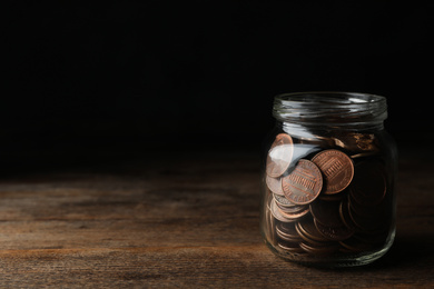 Photo of Glass jar with coins on wooden table, space for text