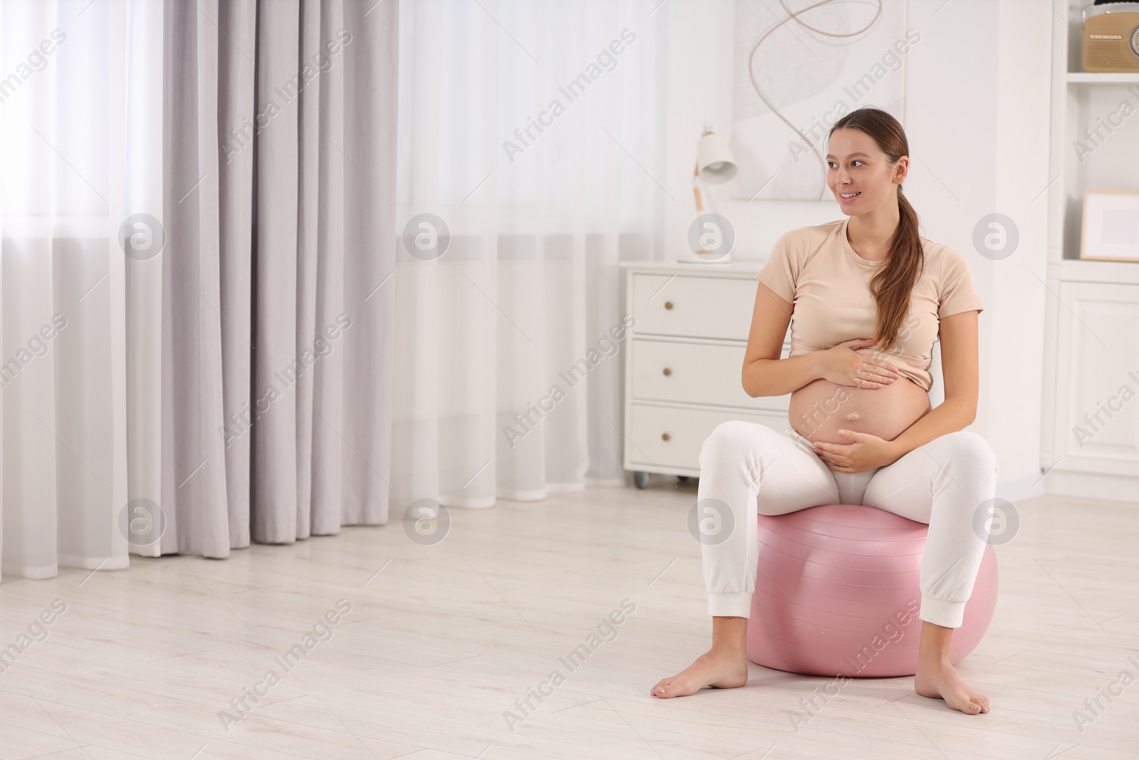 Photo of Pregnant woman sitting on fitness ball at home, space for text. Doing yoga