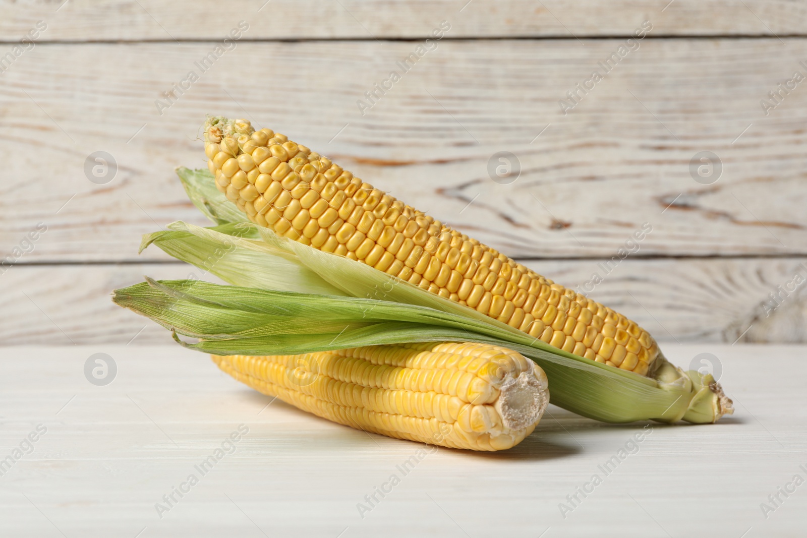 Photo of Ripe corn cobs on white wooden table