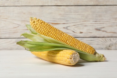 Photo of Ripe corn cobs on white wooden table